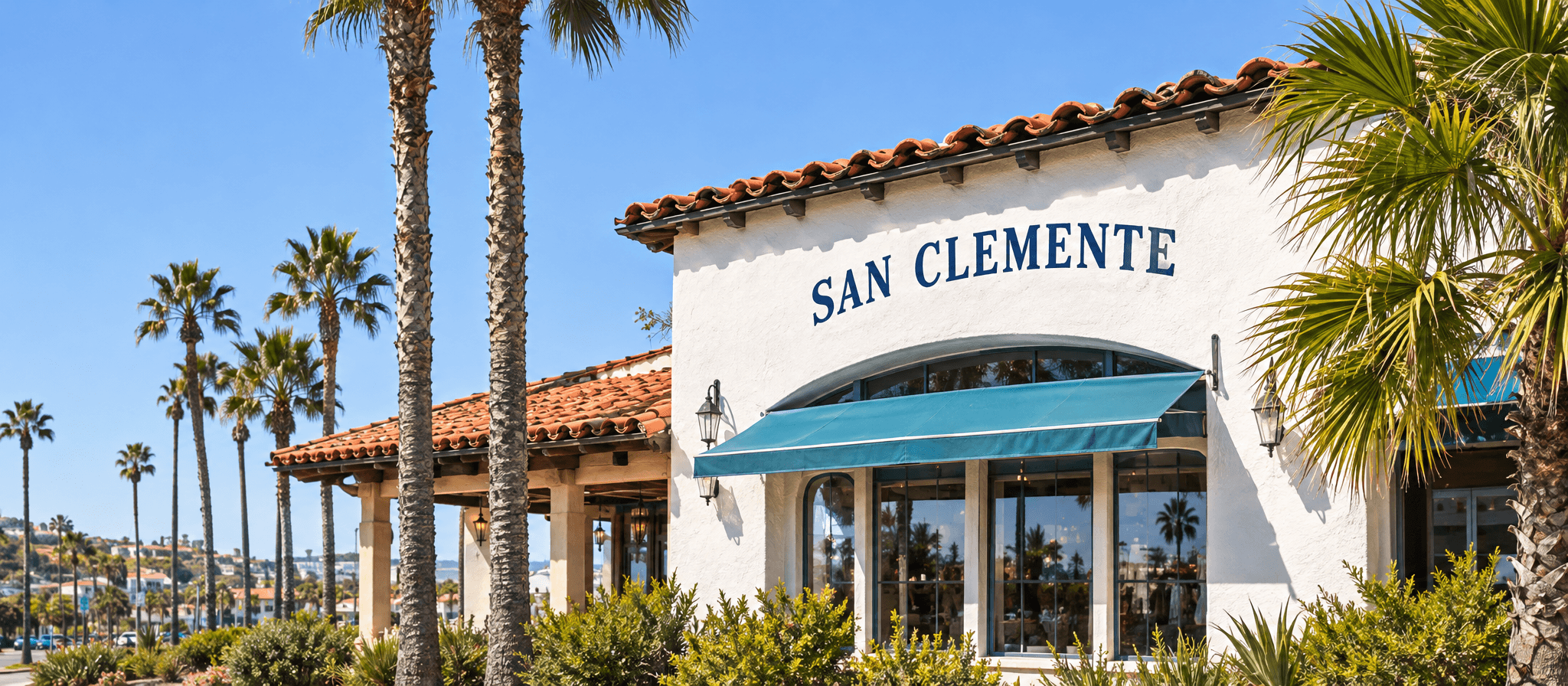 A white Spanish-style storefront with a teal awning under palm trees.